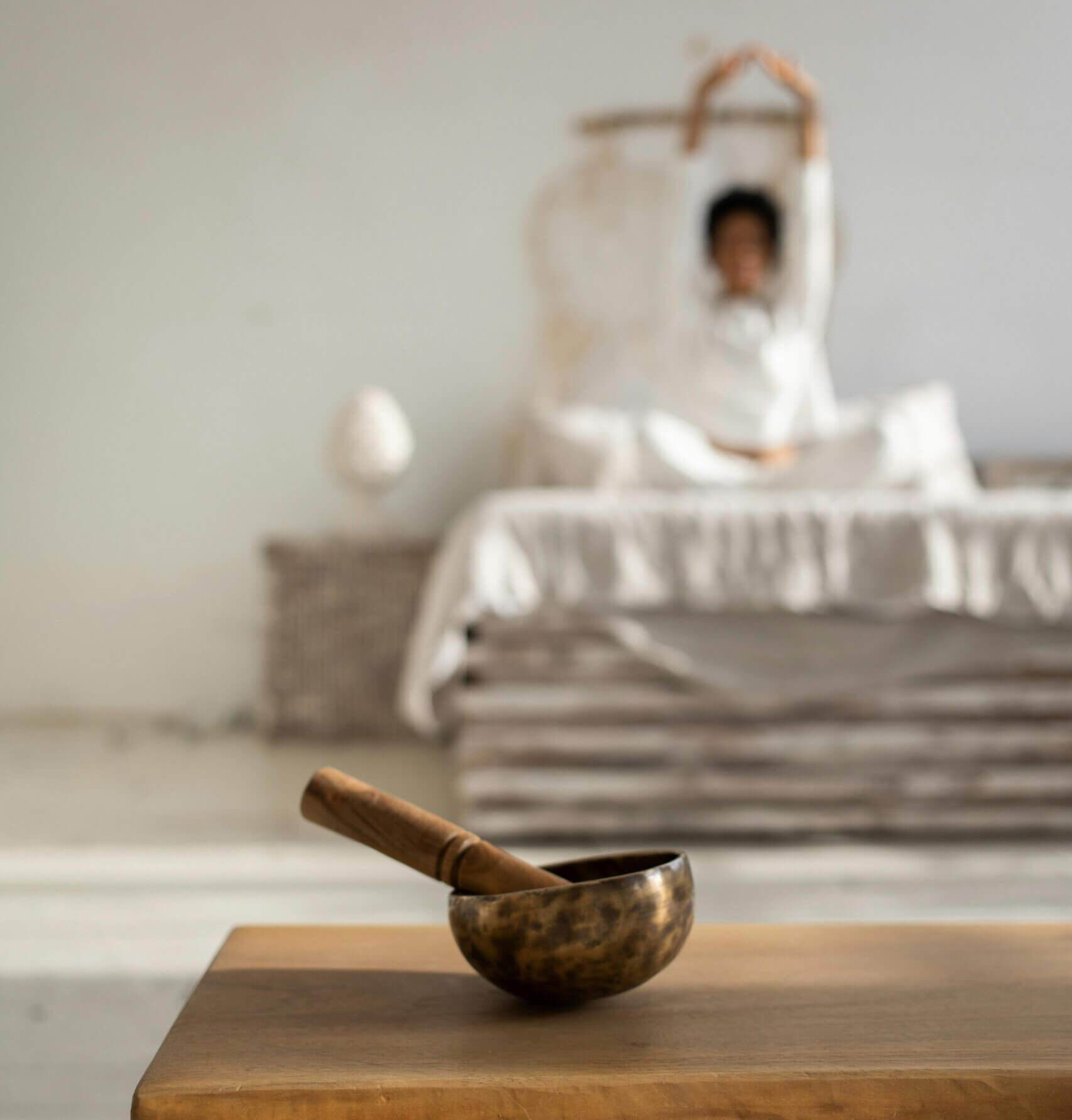 relaxation Une femme floutée au loin sur son lit entrain de s'étirer et au premier plan on voit un bol tibétain.